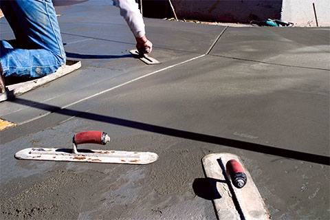 A worker operating a concrete roller to flatten freshly poured concrete.