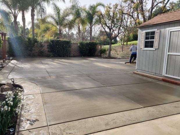A concrete patio with a shed and a fence in a backyard setting.
