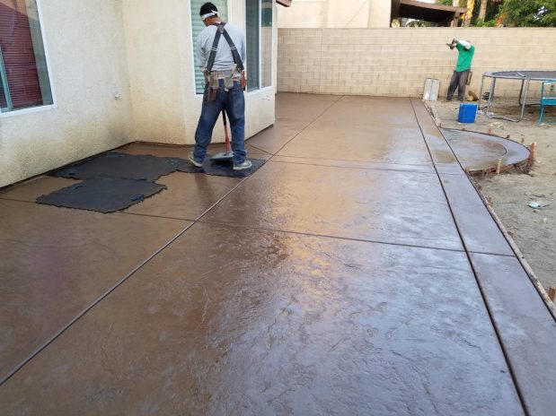 A person laboring on a concrete patio, leveling and finishing the surface with precision.