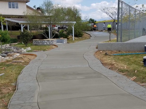 Concrete walkway with fence and house in background.