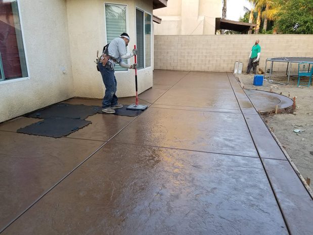 Man sweeping a concrete patio with a broom.