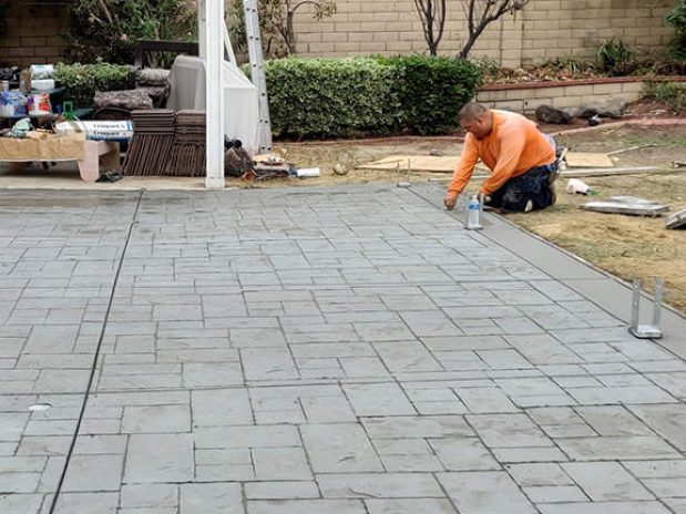 A man laying concrete patio in backyard, using tools and leveling the surface.